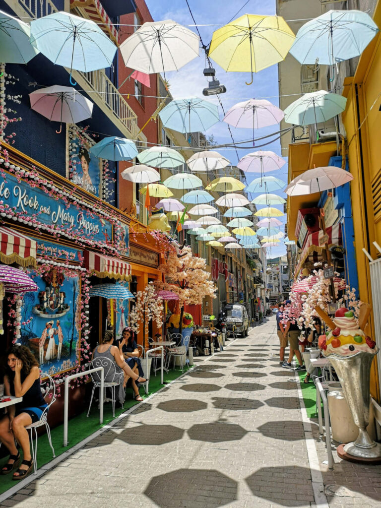 A colorful view of Pittaki Street in Psyrri, featuring the fairytale decor of Little Kook and hanging umbrellas, highlighting the best time to visit Athens 2026 for street culture.